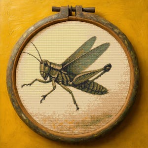 May include: A cross-stitch embroidery of a grasshopper in shades of green, brown, and tan, set within a round wooden embroidery hoop. The grasshopper is detailed with visible wings and legs, against a cream-colored background.