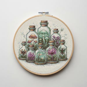 Könnte beinhalten: Kreuzstichkunst mit einer Sammlung von Glasflaschen mit Korken, die jeweils ein anderes botanisches Element enthalten. Die Flaschen sind in einem kreisförmigen Muster in einem hölzernen Stickrahmen angeordnet. Das Kunstwerk zeigt Pilze, Blumen und Insekten.