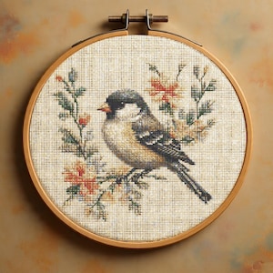 May include: Cross-stitch embroidery of a bird on a flowering branch, framed in a wooden hoop. The bird has a black head, tan body, and grey wings. The flowers are orange and pink, with green leaves. The hoop is approximately 20 cm in diameter.