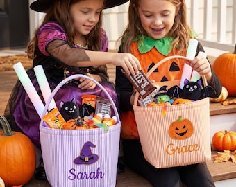Puede incluir: Dos cubos de tela para Halloween con asas. El cubo izquierdo es de rayas moradas con un sombrero de bruja bordado y el nombre Sarah. El cubo derecho es de rayas naranjas con una calabaza bordada y el nombre Grace.