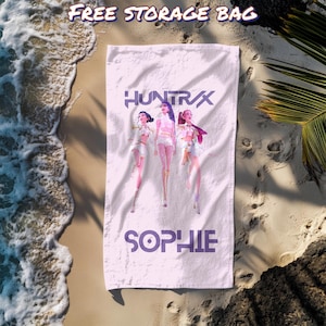 May include: White beach towel with the text "HUNTRAX" and "SOPHIE" in purple. The towel features a graphic of three figures in white and pink outfits. The words "FREE STORAGE BAG" are at the top of the image.
