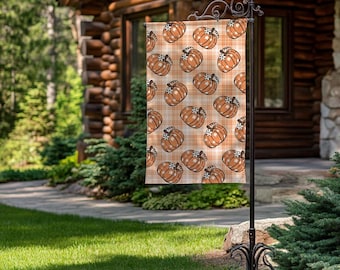 May include: A garden flag with a repeating pattern of orange pumpkins on a plaid background. The flag is displayed on a black metal stand, ideal for autumn decor. The pumpkins have white accents.