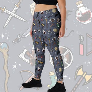 May include: Grey leggings with a repeating pattern of fantasy role-playing game icons, including swords, potions, dice, and staffs.