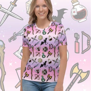 May include: A white t-shirt with a pink and purple ombre background. The shirt features a repeating pattern of various fantasy and role-playing game icons, including swords, axes, potions, dice, and dragons.