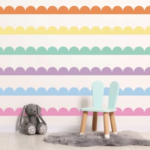 May include: A wall decorated with colorful scalloped stripes in orange, yellow, mint green, purple, light blue, and pink. A light blue chair with wooden legs and a gray stuffed bunny sit in front of the wall.