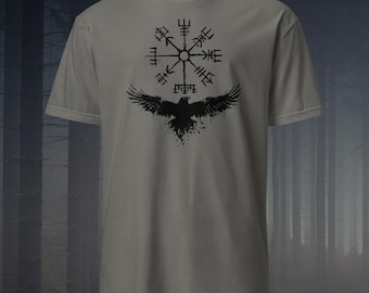Pode incluir: Camiseta cinza com um desenho preto de uma bússola viking e um corvo com as asas abertas. O design está centrado na frente. A camiseta tem gola redonda e mangas curtas. O estilo é simples e marcante.