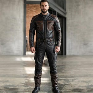 Op de afbeelding: Zwart en bruin leren motorpak met een jas met ritssluiting en bijpassende broek. De jas heeft bruine schouder- en borstaccenten en de broek heeft cargozakken. Het pak is in de taille voorzien van een riem en wordt gedragen met zwarte laarzen.