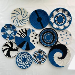 Peut inclure: Un ensemble de dix paniers muraux circulaires en corde tressée dans des tons de bleu, noir et blanc. Chaque panier présente un motif géométrique unique, incluant des spirales, des rayures radiales, des motifs floraux et des designs à carreaux.