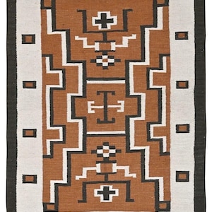 May include: Rectangular woven rug with a geometric pattern in brown, white, and black. The rug features a central brown section with white and black geometric shapes, framed by a white border and a black outer edge. The rug measures 5'11" x 4'.