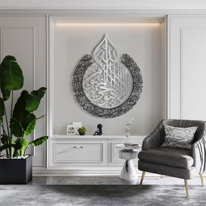 May include: A white and black metal wall art piece featuring Arabic calligraphy in a circular design. The art piece is hanging on a white wall in a modern living room.