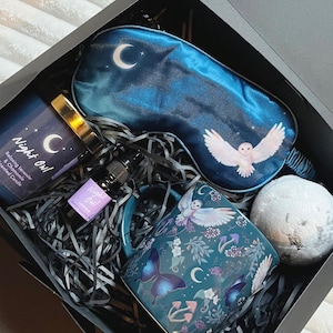 May include: A black gift box filled with a blue sleep mask, a teal mug with an owl and butterfly design, a lavender scented candle, a bottle of lavender oil, and a bath bomb. The candle and oil are labeled "Night Owl".