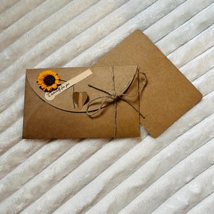May include: A brown envelope with a sunflower and a heart-shaped tag that says "Exclusively for you". The envelope is tied with twine and has a second brown envelope behind it.