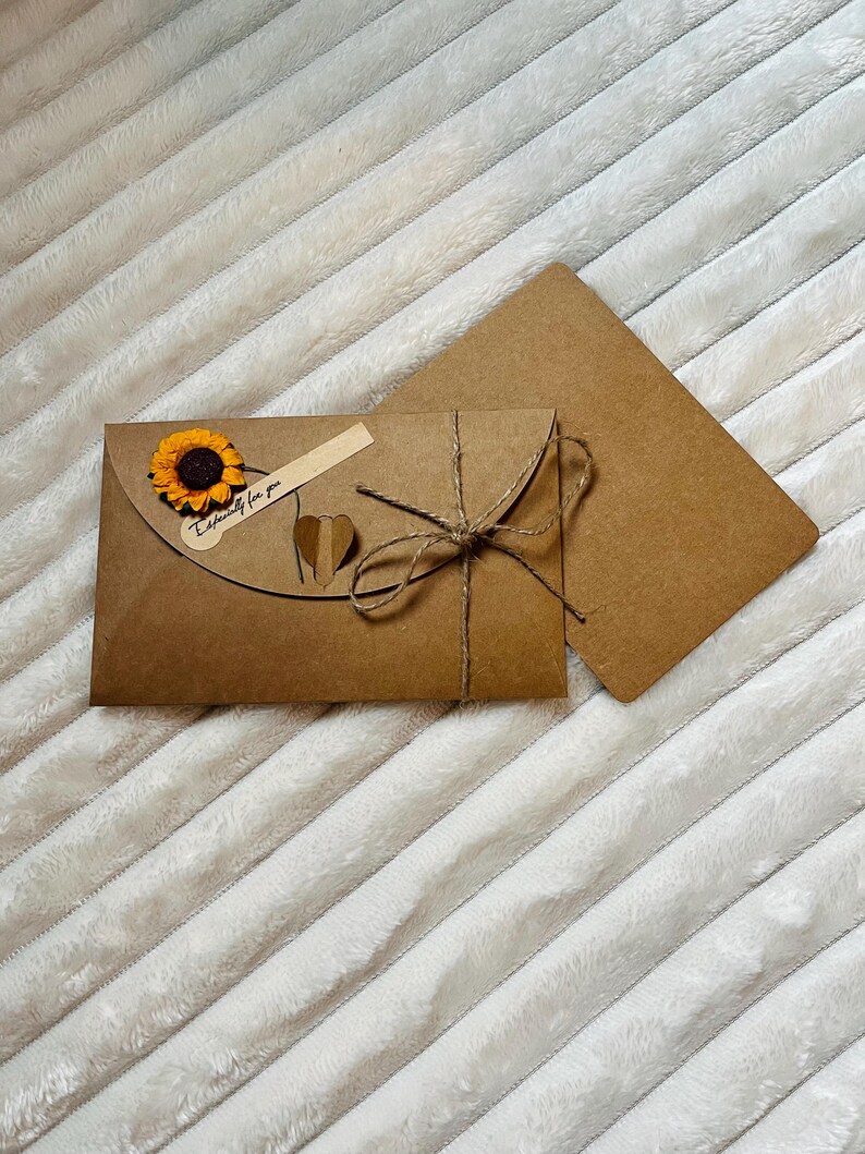 May include: A brown envelope with a sunflower and a heart-shaped tag that says "Exclusively for you". The envelope is tied with twine and has a second brown envelope behind it.