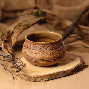 Könnte beinhalten: Eine braune Keramikschüssel mit einem wellenförmigen und kreisförmigen Design. Die Schüssel steht auf einer Holzscheibe.