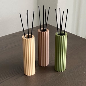 Può includere: Tre bottiglie per diffusore cilindriche con canne nere. Le bottiglie sono realizzate in materiale testurizzato e sono di colore beige, marrone e verde.