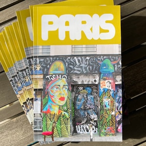 May include: A stack of yellow magazines with the word "PARIS" printed in white on the cover. The cover image shows a colorful street art mural with a woman's face, a blue bird, and a green creature.
