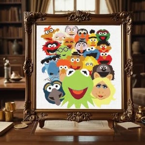 Könnte beinhalten: Ein gerahmtes Kreuzstichbild mit einer farbenfrohen Collage von Muppet-Charakteren. Das Kunstwerk zeigt Kermit den Frosch, Miss Piggy und andere beliebte Charaktere. Der Rahmen ist verziert, mit dunkler brauner Oberfläche, und steht auf einem Holzschreibtisch.