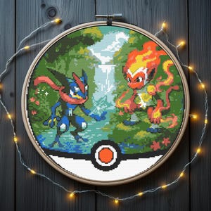 May include: A cross-stitch embroidery featuring two Pokémon characters in a forest scene, set within a wooden hoop. The design includes a waterfall and a Poké Ball at the bottom. The background is a dark wooden surface with string lights.
