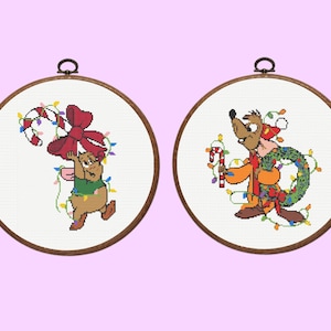 Puede incluir: Dos obras de arte de punto de cruz enmarcadas y redondas. Una presenta un personaje de dibujos animados sosteniendo un bastón de caramelo y un gran lazo rojo, adornado con luces navideñas. La otra representa un perro de dibujos animados con una corona y un bastón de caramelo, también con luces.