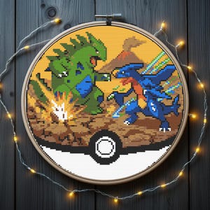 Puede incluir: Arte de aro de punto de cruz que representa una escena de batalla pixelada entre dos personajes Pokémon. Uno es verde y azul, el otro azul y naranja, sobre un cielo amarillo con un volcán. El diseño está enmarcado en un aro de madera, con luces de hadas.