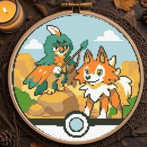 May include: A circular embroidery hoop containing a cross-stitch pattern of two stylized creatures. One creature is green and orange with a spear, and the other is orange and white. A circular icon with a light blue center sits at the bottom.