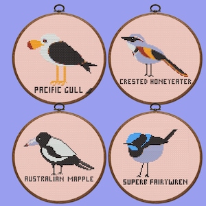 May include: Four embroidery hoops with pink fabric and brown wooden frames. Each hoop features a different Australian bird: a Pacific Gull, a Crested Honeyeater, an Australian Magpie, and a Superb Fairy Wren. The bird's names are embroidered below each image.