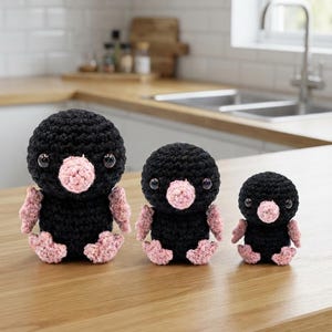 May include: Three handmade crochet mole dolls in descending sizes, each featuring a round black body, a textured pink nose, small pink feet, and shiny black plastic eyes. The figures are arranged in a row, showcasing a consistent design.