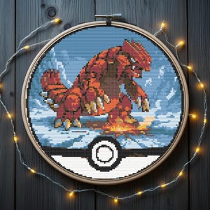 May include: A cross-stitch embroidery of a red and orange creature, set against a blue and white snowy background, within a wooden hoop. The design is set inside a black and white Pokeball. The piece is decorated with fairy lights.