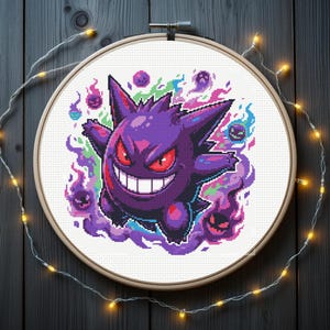 Könnte beinhalten: Ein Kreuzstich-Stickrahmen mit einer lila Cartoonfigur mit breitem Grinsen und roten Augen, umgeben von bunten Flammen und kleineren geisterhaften Figuren. Das Design befindet sich auf einem weißen Stoffhintergrund, der von einem Holzrahmen umgeben und mit Lichterketten verziert ist.