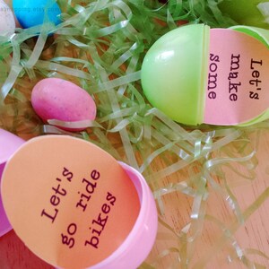 May include: Two plastic Easter eggs with messages inside. One egg is pink and says "Let's go ride bikes". The other egg is green and says "Let's make some".