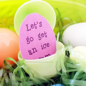May include: A pink paper note with the text "Let's go get an ice cream" inside a plastic Easter egg. The egg is surrounded by green and white shredded paper.