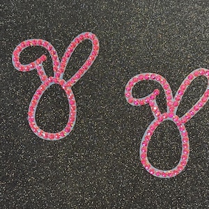 May include: Two pink bunny shaped rhinestone iron-on patches.