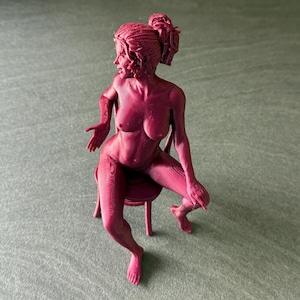 May include: A monochromatic dark pink 3D printed figurine of a person with a ponytail, seated on a small stool. The figure is depicted in a seated pose with one arm extended to the side and the other resting on a leg, showing visible layer lines.