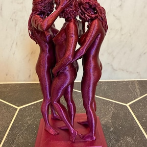 May include: A 3D printed sculpture in a metallic magenta finish depicting three figures standing in a circle, facing inward with their arms intertwined. The figures are positioned on a square base, showcasing a textured, layered surface.