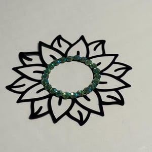 May include: A black and white sunflower outline with a circle of green iridescent rhinestones in the centre.