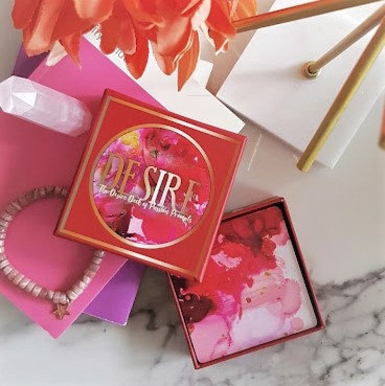 May include: A red box with a gold circle containing the word "DESIRE" and the text "The Oracle Deck of Passion & Purpose". The box is open and the deck of cards is visible with a pink, red, and yellow abstract design.