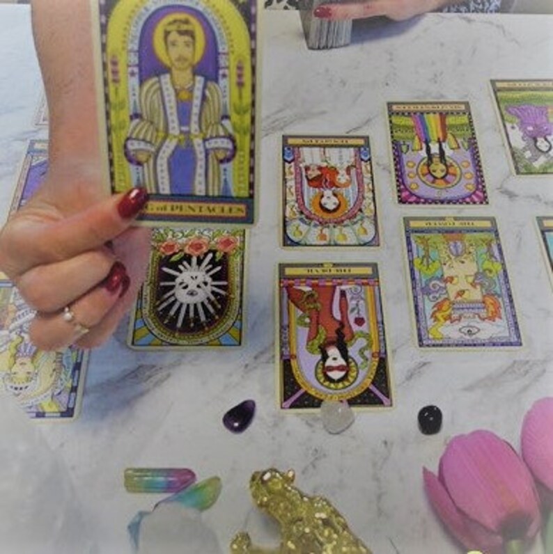 May include: A tarot card reading spread with several cards laid out on a white surface. The cards are colorful and feature illustrations of people and symbols. The cards include "The Emperor of Pentacles", "The Star", "The Lovers", "The World", and "Justice".