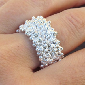 Könnte beinhalten: Ein silberner Ring mit einer strukturierten Oberfläche aus kleinen, runden Perlen.