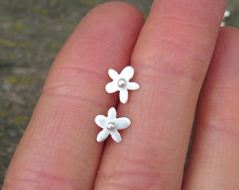Op de afbeelding: Een paar zilveren bloem oorbel studs met een klein parel centrum.