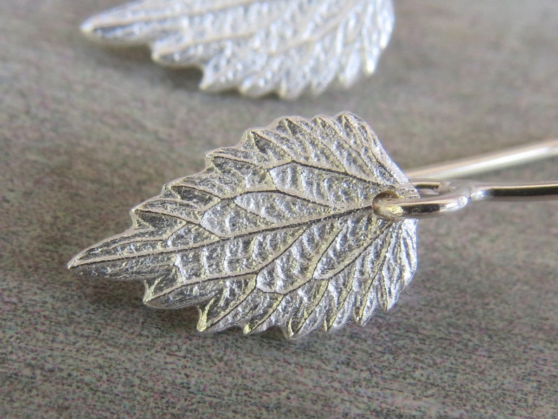 May include: A pair of silver earrings featuring a detailed leaf design. The leaves are textured and have a delicate, organic look.