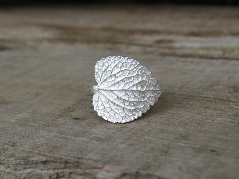 May include: A silver ring shaped like a leaf with a detailed, textured surface.