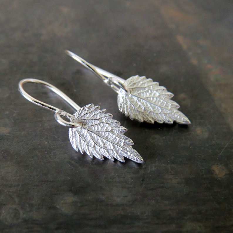 May include: A pair of silver earrings shaped like leaves. The leaves have a detailed, textured surface.