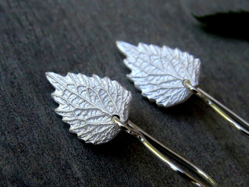 May include: A pair of silver earrings shaped like leaves. The leaves have a detailed, textured design.