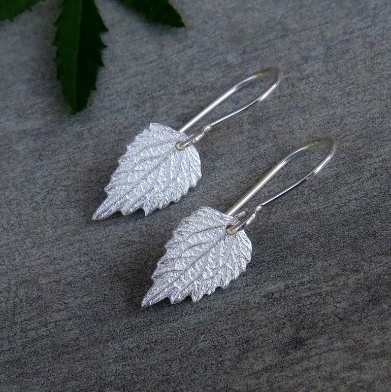 May include: A pair of silver earrings with a leaf design. The leaves are textured and have a delicate, organic look.