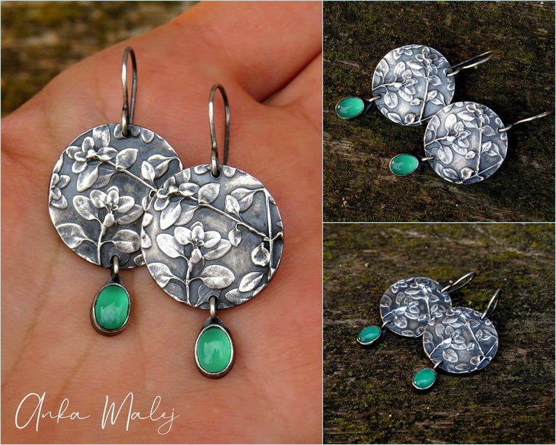 Puede incluir: Pendientes de plata con dise&ntilde;o floral y gotas de piedras preciosas verdes. Los pendientes se muestran en una mano y sobre una superficie de madera.