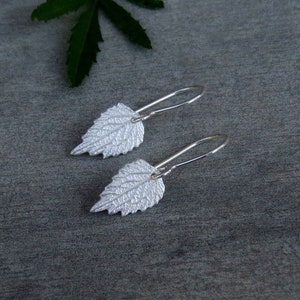 May include: A pair of silver earrings shaped like leaves. The leaves have a textured surface and are attached to silver hooks.