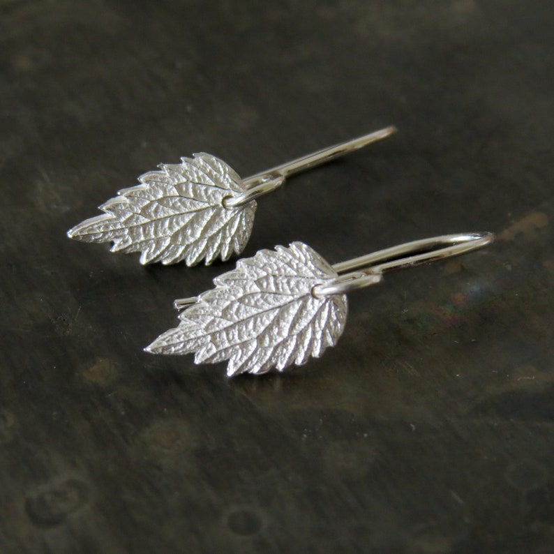 May include: A pair of silver earrings with a leaf design. The leaves are textured and have a delicate, organic look.