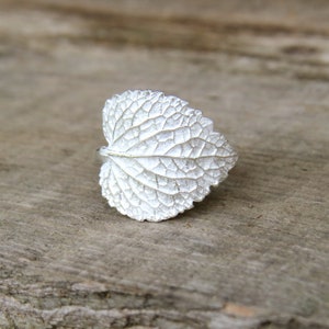 May include: A silver ring shaped like a leaf with a detailed textured surface.