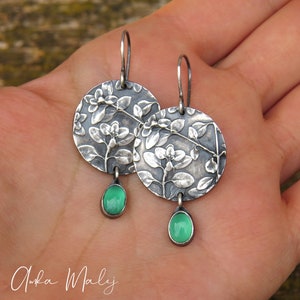 Puede incluir: Pendientes de plata con dise&ntilde;o floral y detalles de piedras preciosas verdes.