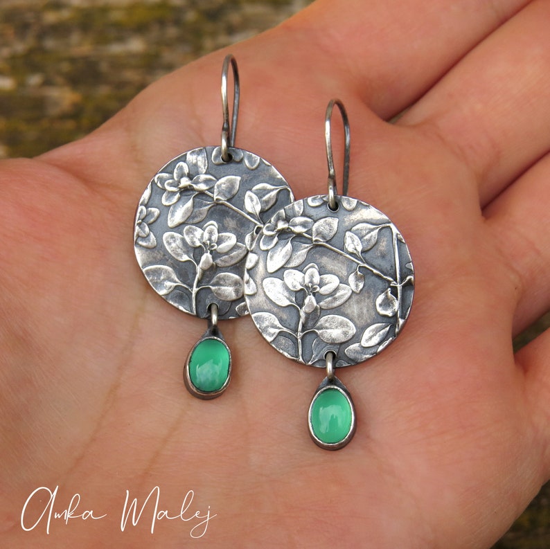 Puede incluir: Pendientes de plata con dise&ntilde;o floral y detalles de piedras preciosas verdes.